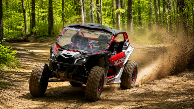 2026 Can-Am Maverick X3 X DS Turbo RR with Smart-Shox driving through a wooded off-road trail and kicking up dust